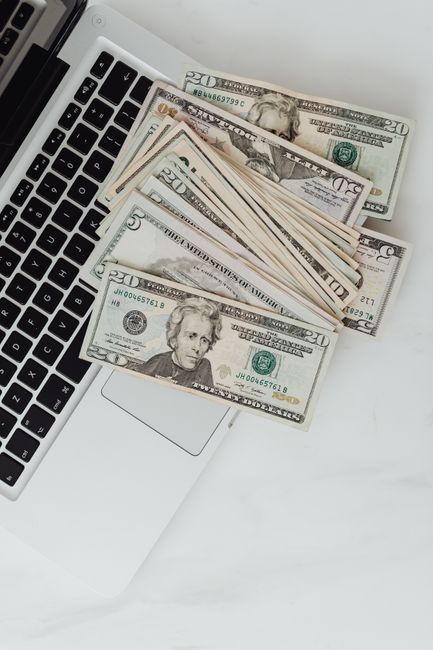 US dollar banknotes scattered over a laptop, symbolizing online finance and digital banking. US dollar banknotes scattered over a laptop, symbolizing online finance and digital banking.