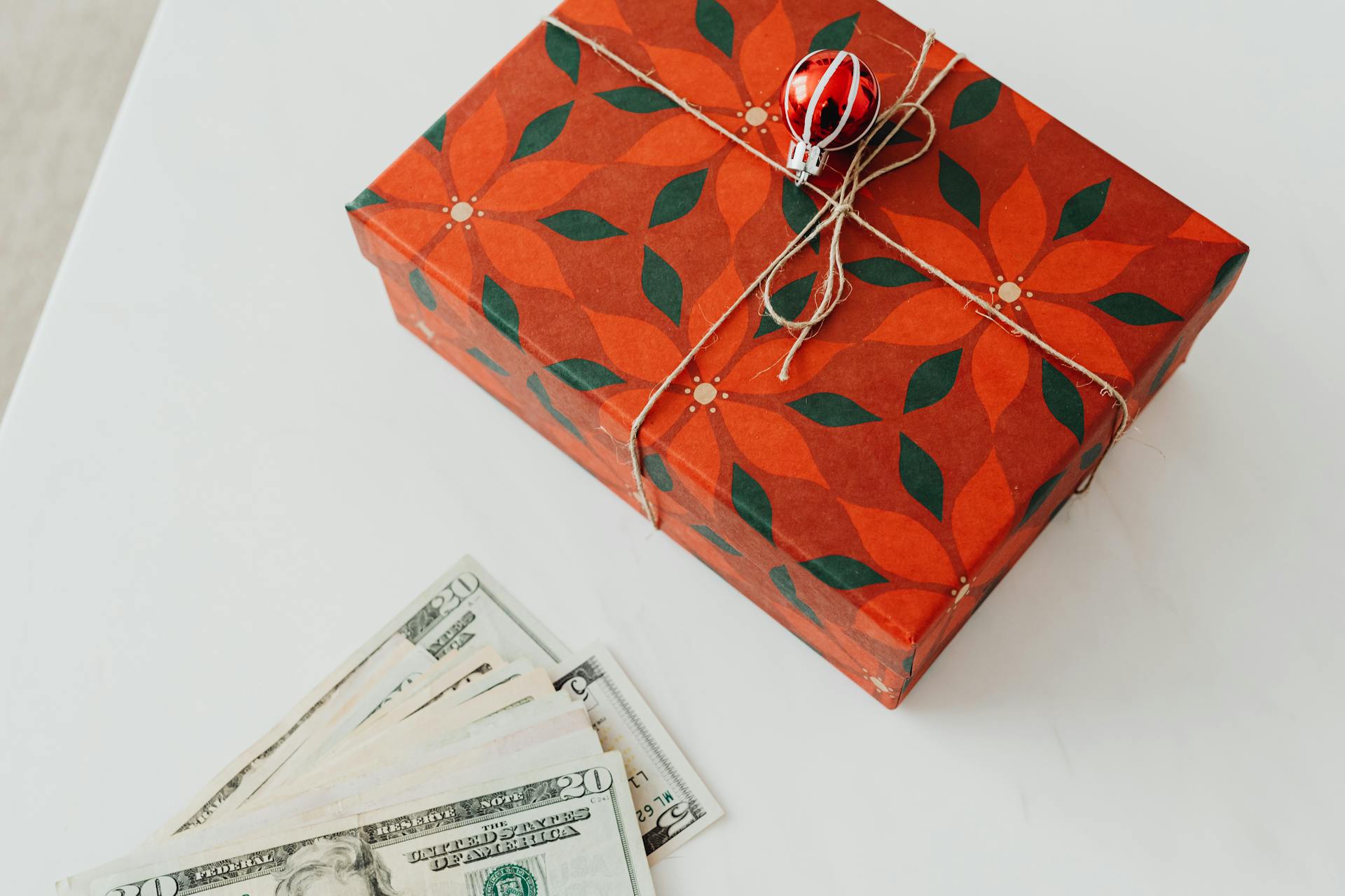 Christmas-themed gift box tied with string and banknotes nearby on a white surface.