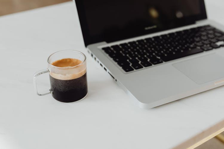 Cup Of Coffee Standing By Open Laptop