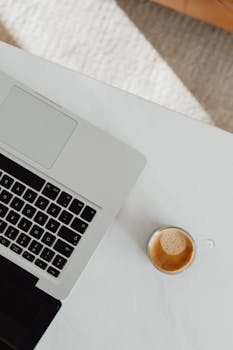 A minimalist top view of a laptop and a cup of coffee on a white desk, perfect for productivity and technology themes.