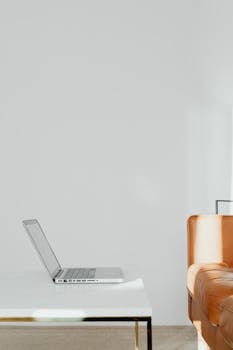 Minimalist design featuring a laptop on a white table in a modern home with a leather sofa.
