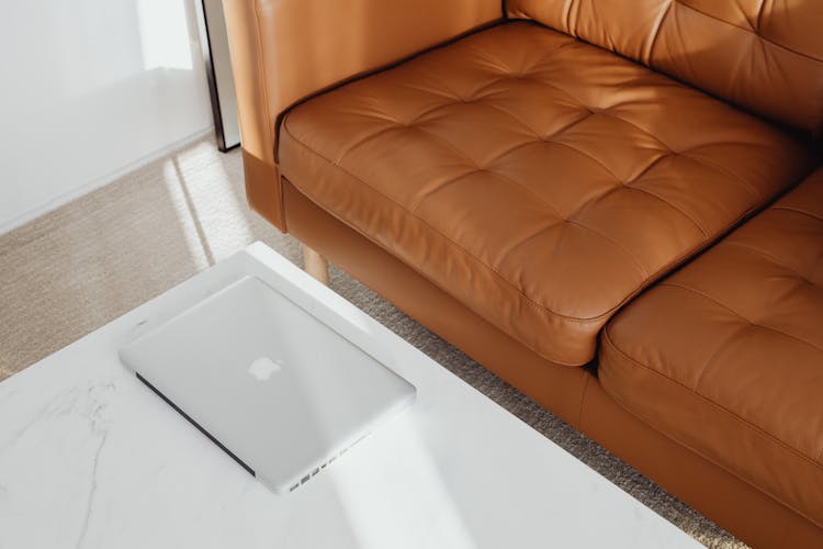 Laptop On A Table Next To A Brown Leather Couch