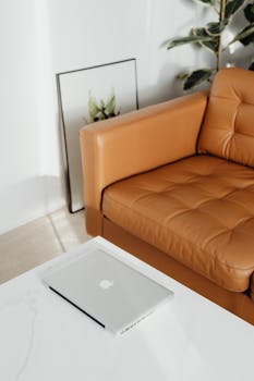 A sleek laptop rests on a marble table beside a tan leather sofa in a stylish living room.