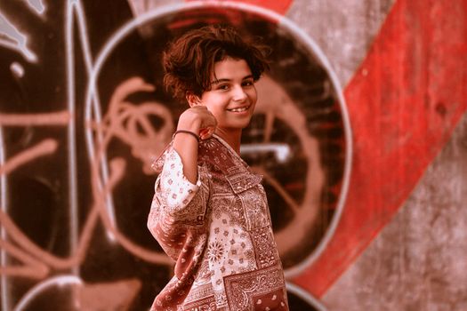 Portrait of a smiling woman posing confidently in front of a vibrant graffiti mural with a stylish blouse.