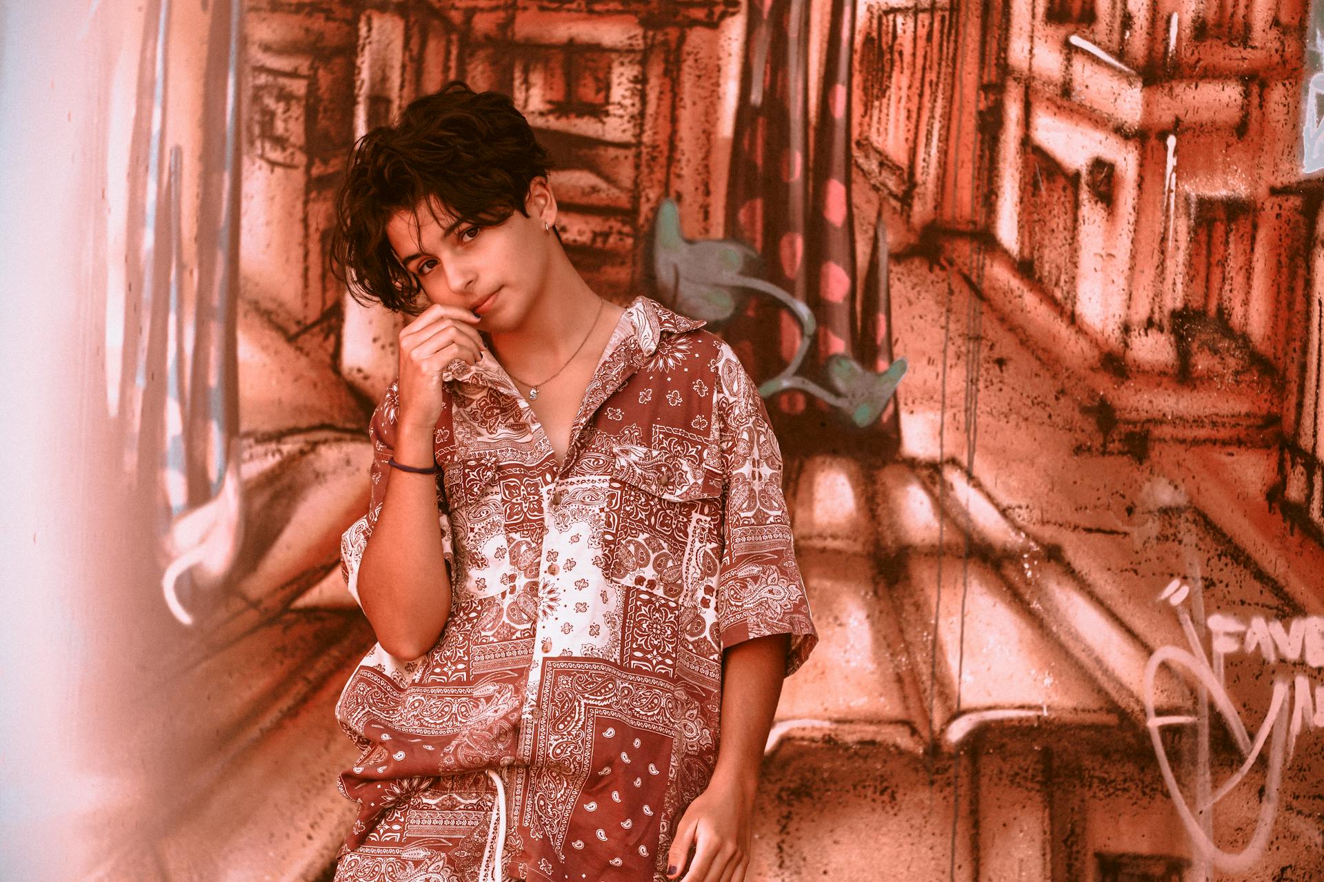 A stylish teenage boy poses thoughtfully against a colorful graffiti wall, blending art and fashion.
