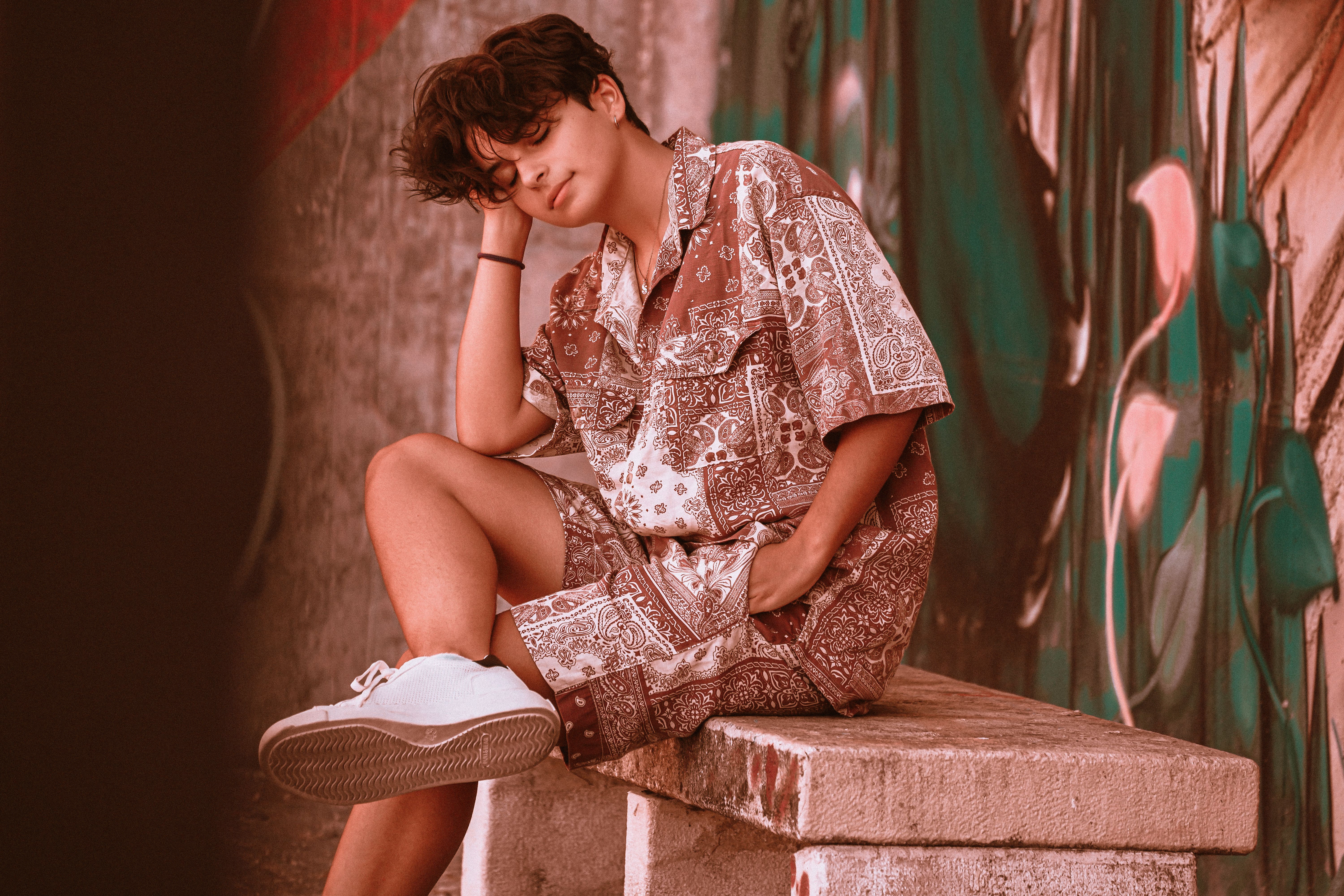 Teenage boy sitting on a bench, eyes closed, wearing a patterned outfit, lost in thought.