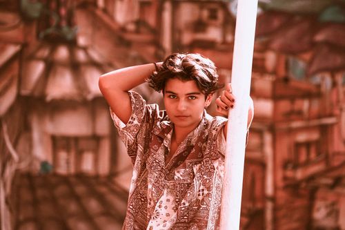 Free Youthful portrait of a teenager with hand in hair, standing against a cityscape background. Stock Photo
