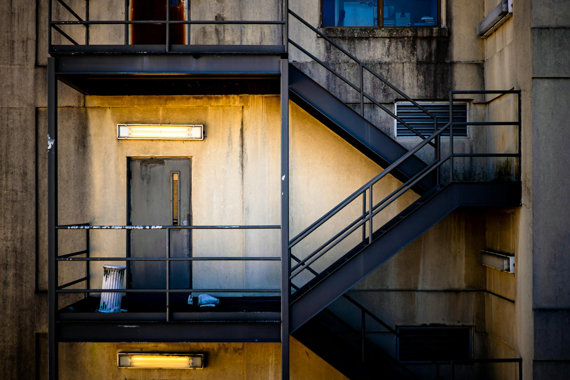 A detailed view of an apartment fire escape staircase with rusty door and lighting.