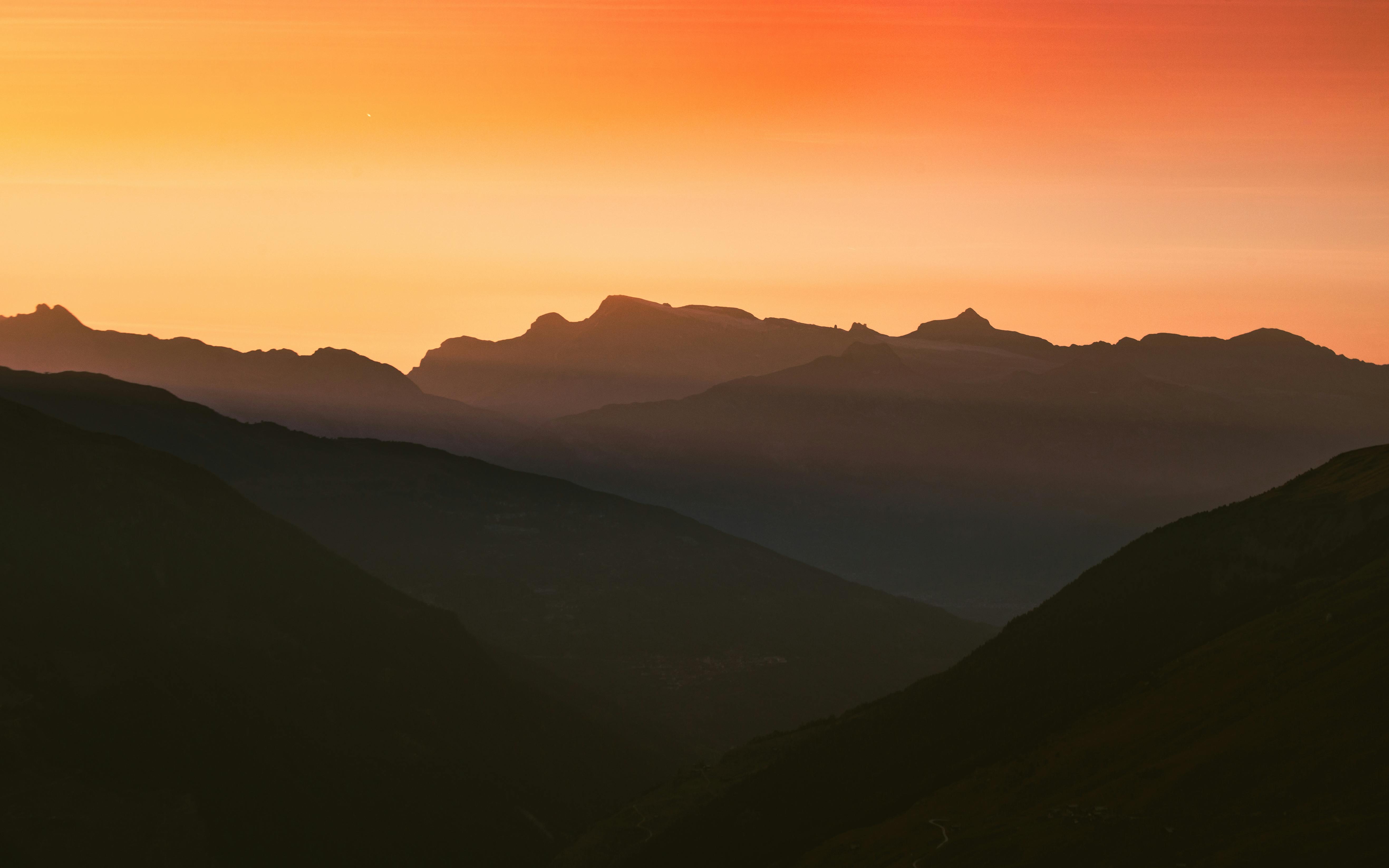 Stunning silhouette of Swiss mountains under a vibrant sunset sky.