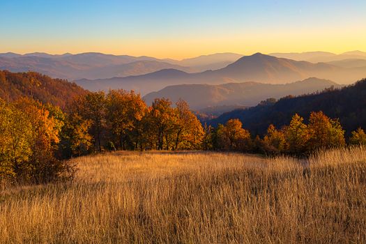 Breathtaking view of mountains at sunset with autumn foliage and golden fields.