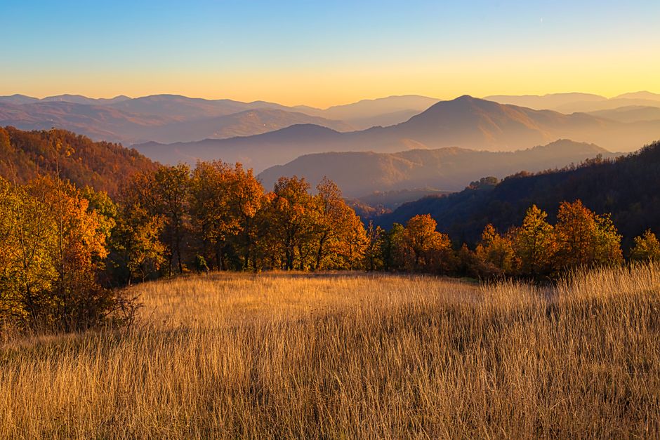 Breathtaking view of mountains at sunset with autumn foliage and golden fields.
