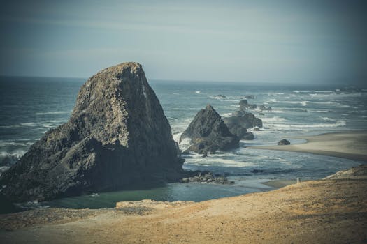 Majestic coastal cliffs meeting the ocean with crashing waves under a clear sky, captured in a moody tone.
