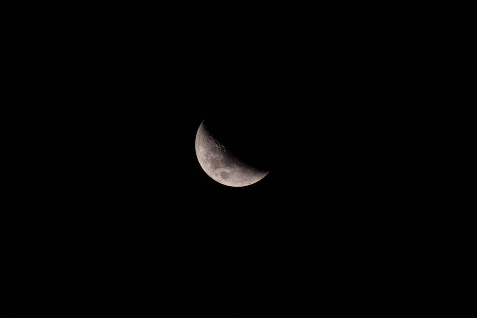Bright crescent moon with craters shining high in air on black background of dark sky in night time in atmosphere