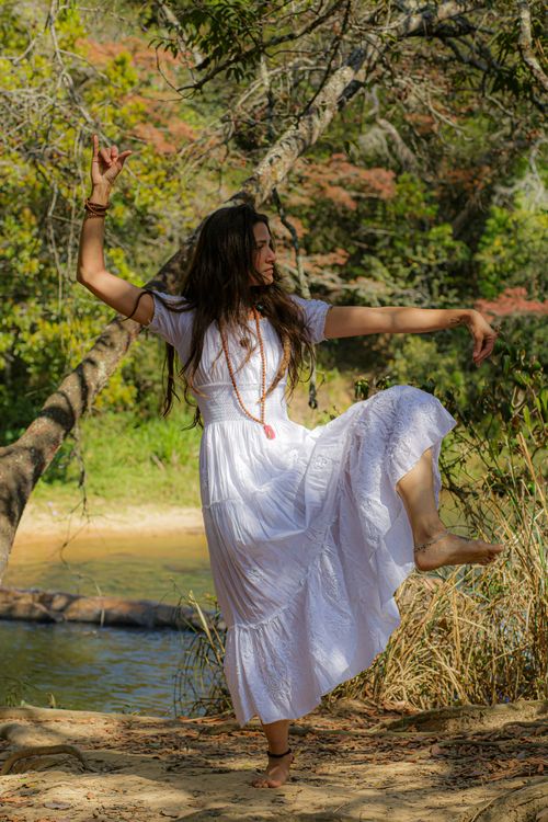 Free Full body of barefoot female in white long dress and traditional accessories standing on sandy lakeside near water while dancing in nature Stock Photo