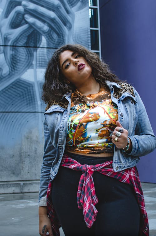 Young confident ethnic plus size lady in casual clothes standing near blue graffiti wall in city street and looking at camera in day