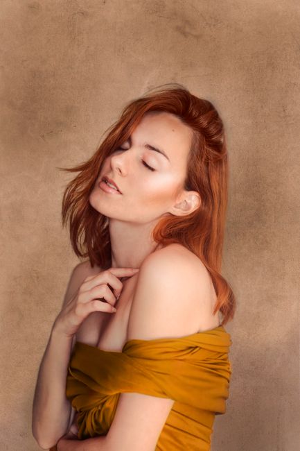 Artistic portrait of a redheaded woman posing gracefully in an off-shoulder outfit.