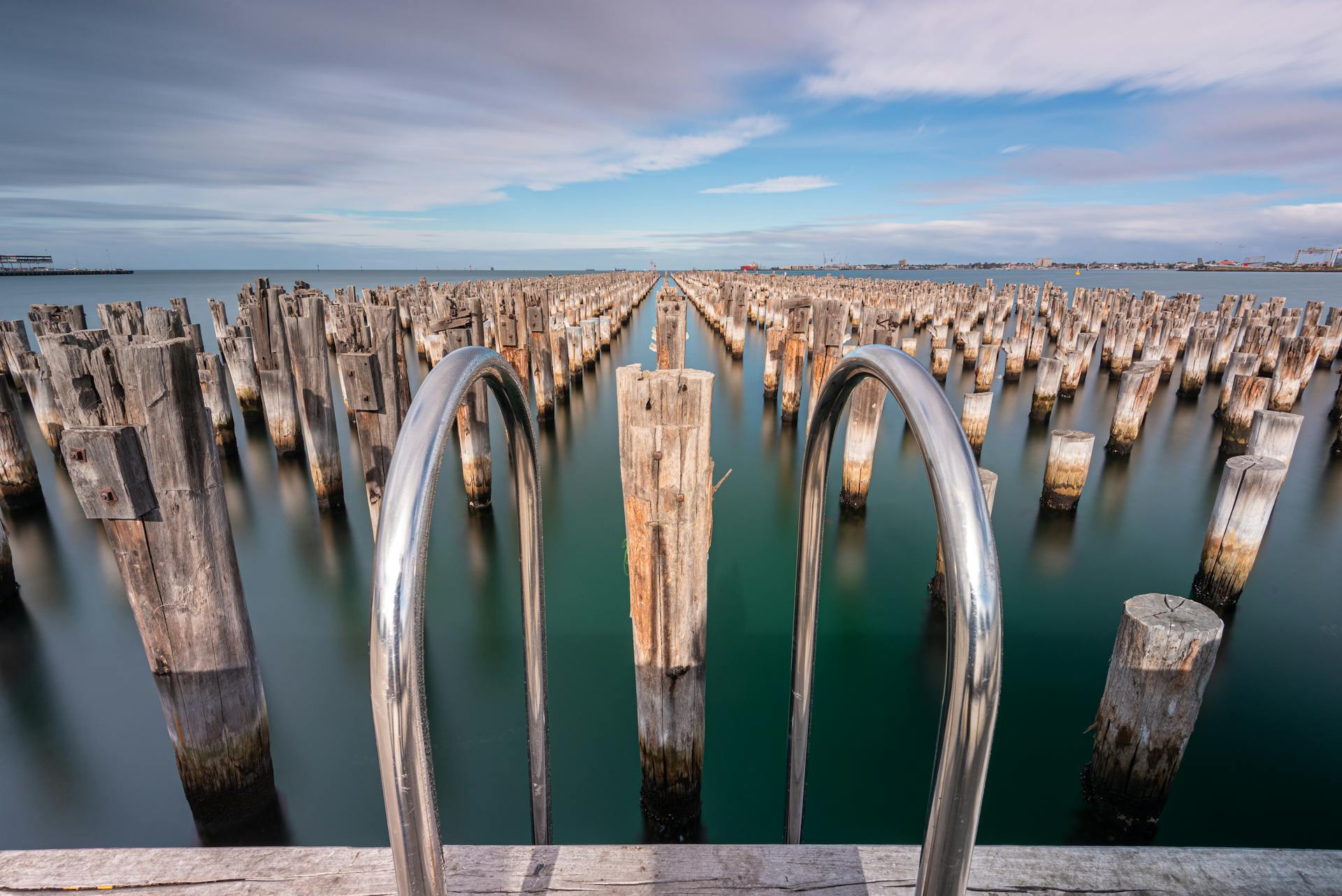 View of weathered wooden posts at Port Melbourne Pier with a steel railing in the foreground.