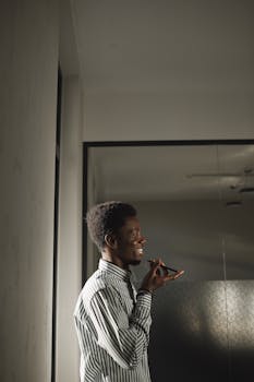 A cheerful man in a striped shirt uses voice command on his smartphone indoors.