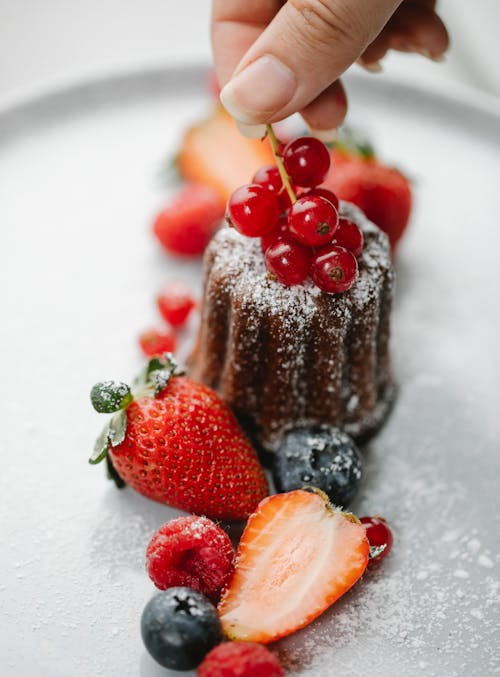 Free From above of crop anonymous female chef adding berries to cake served on plate with strawberries raspberries and blueberries Stock Photo