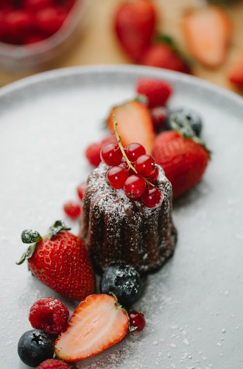 From above of yummy cake decorated with redcurrant berries served on plate with strawberries and blueberries placed on table with blurred background