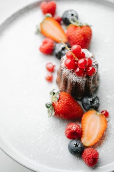 From above of appetizing pie decorated with redcurrant served on white plate with sprinkled sugar and arranged berries with blurred background