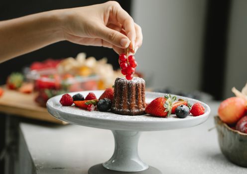 Crop woman decorating cake with berries