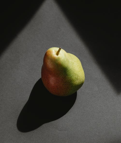 From above of ripe fresh green pear with shadow from daylight on gray background