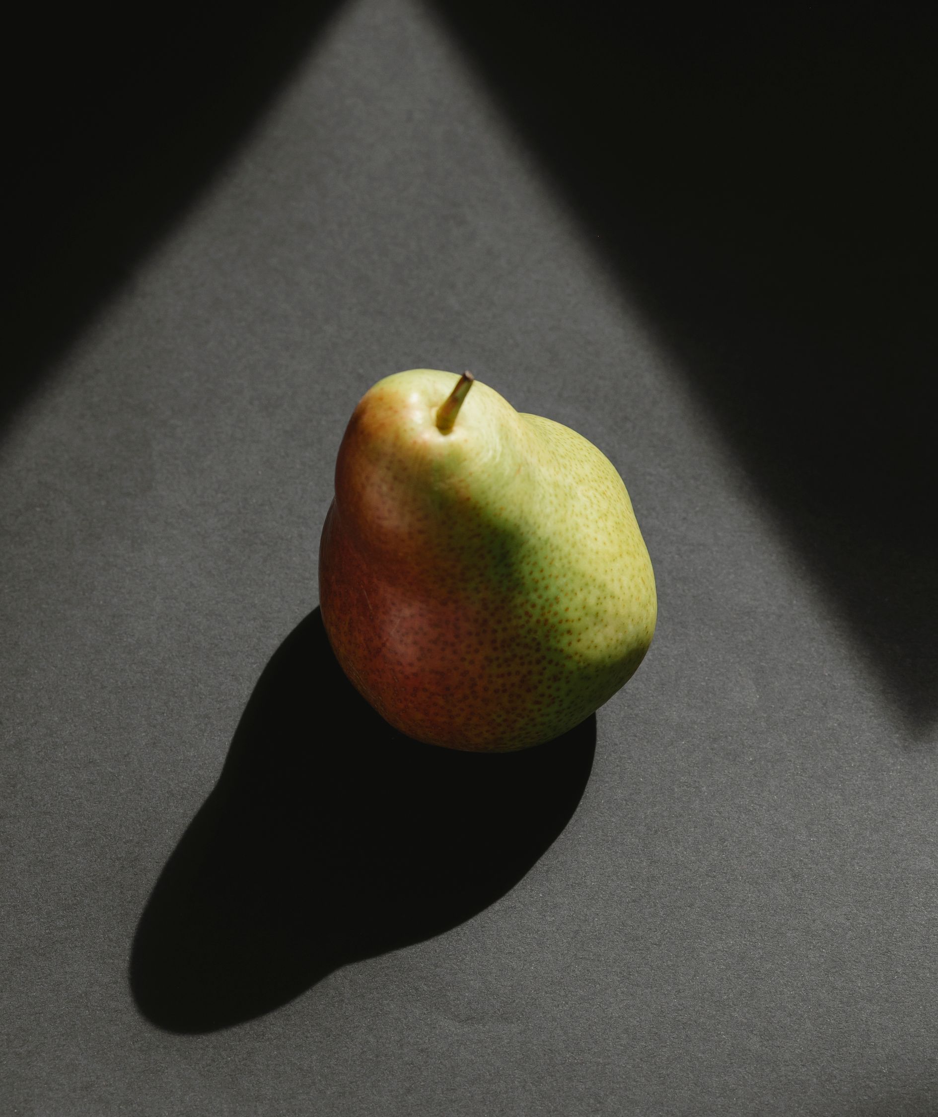 Ripe whole pear casting shadow on gray surface · Free Stock Photo