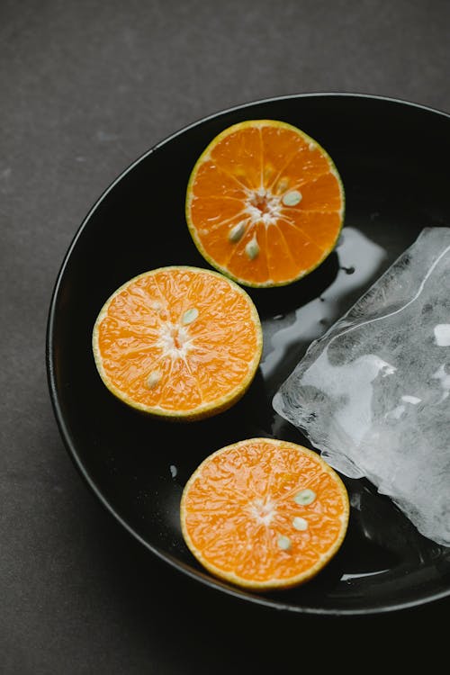 From above of halves of oranges in ceramic bowl with ice representing concept of healthy food