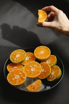 From above crop anonymous person demonstrating slice of fresh ripe orange under bowl with delicious fruits with melting ice