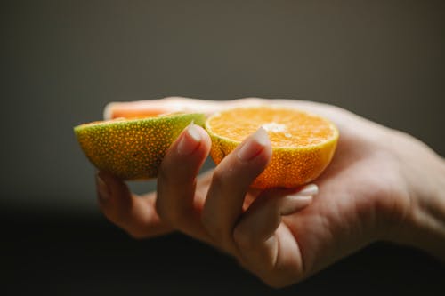 Crop faceless woman showing halves of fresh orange with juicy pulp for healthy diet