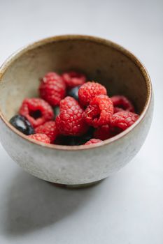 白色桌子上放着碗中新鲜美味的乌藨子和蓝莓，制成健康膳食