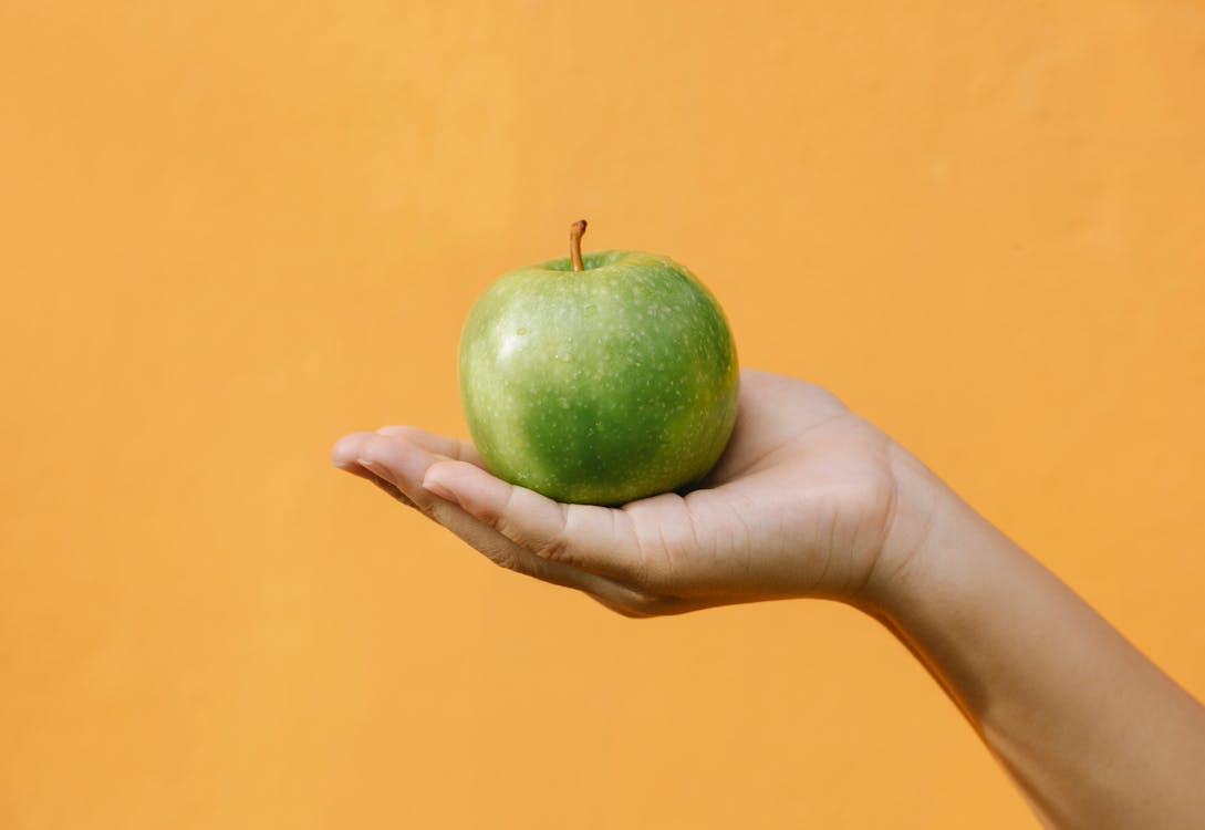 Crop anonymous female demonstrating fruit with thin green skin and crisp flesh against orange background