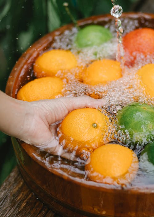 Person washing fresh oranges in wooden bowl