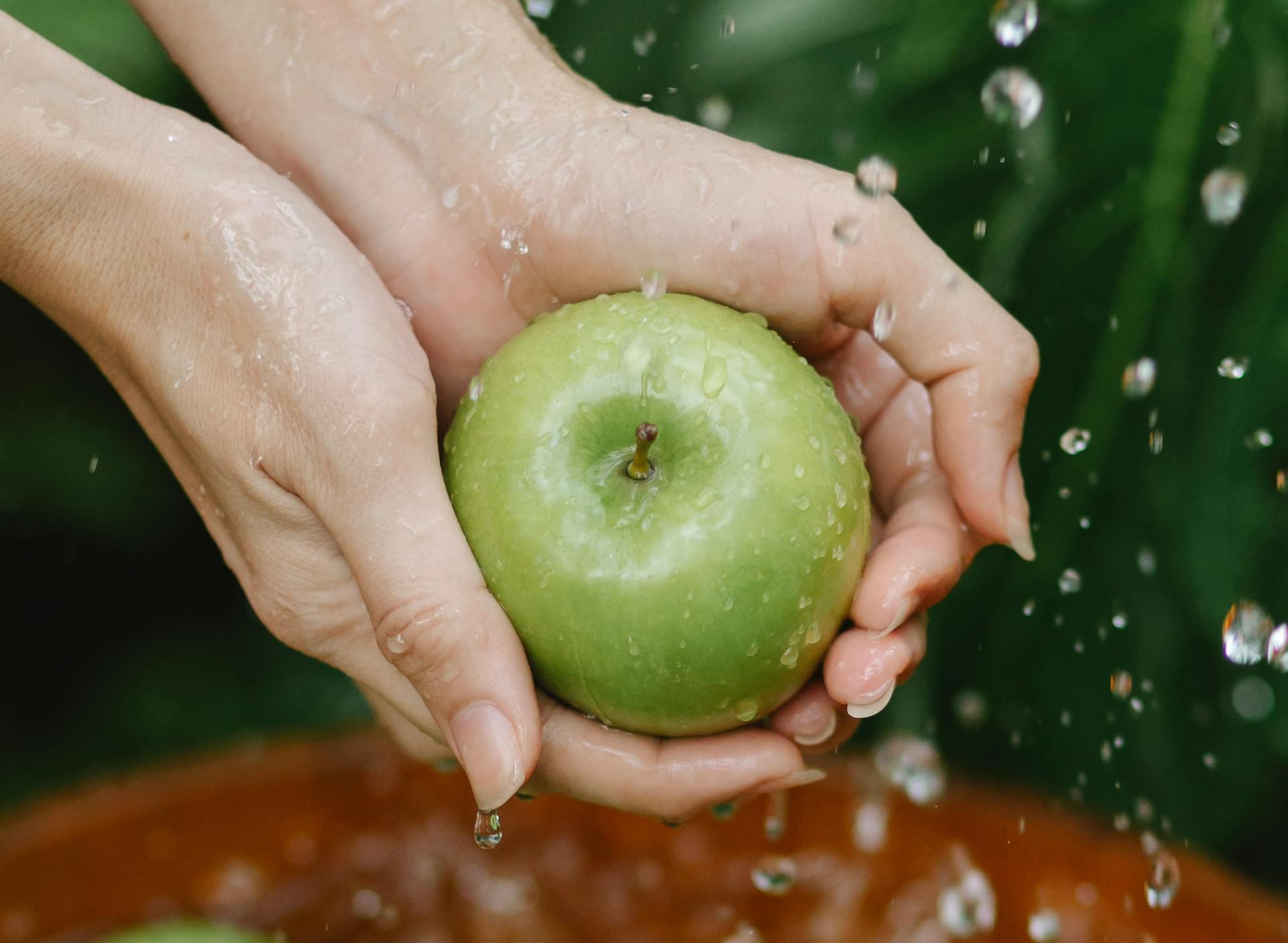 Crop anonymous woman washing green apples in wooden bowl