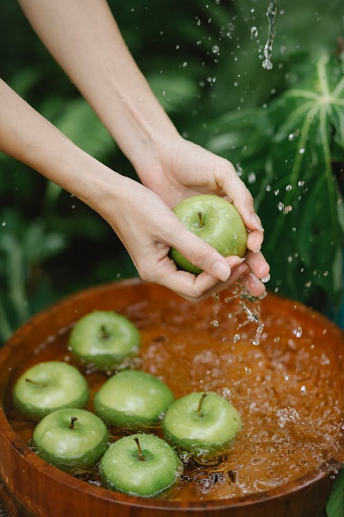Crop woman washing green apples in wooden basin in garden