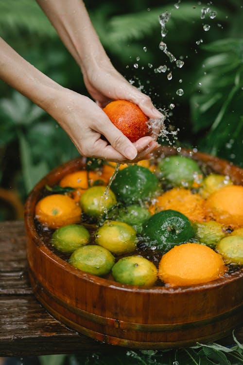 Free From above of crop anonymous young lady washing fresh ripe citrus fruits in wooden basin placed on table in tropical garden Stock Photo