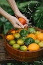 From above of crop anonymous young lady washing fresh ripe citrus fruits in wooden basin placed on table in tropical garden