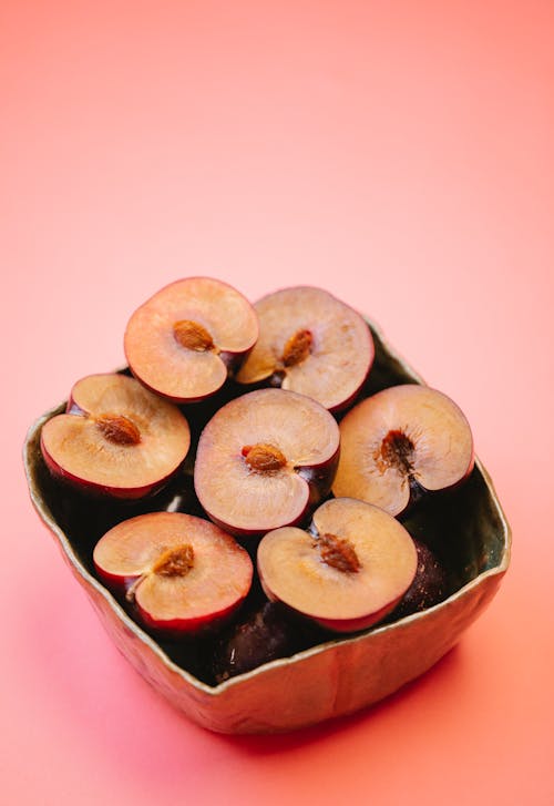 From above heap of ripe fresh sweet halved plums in metal bowl placed on pink surface