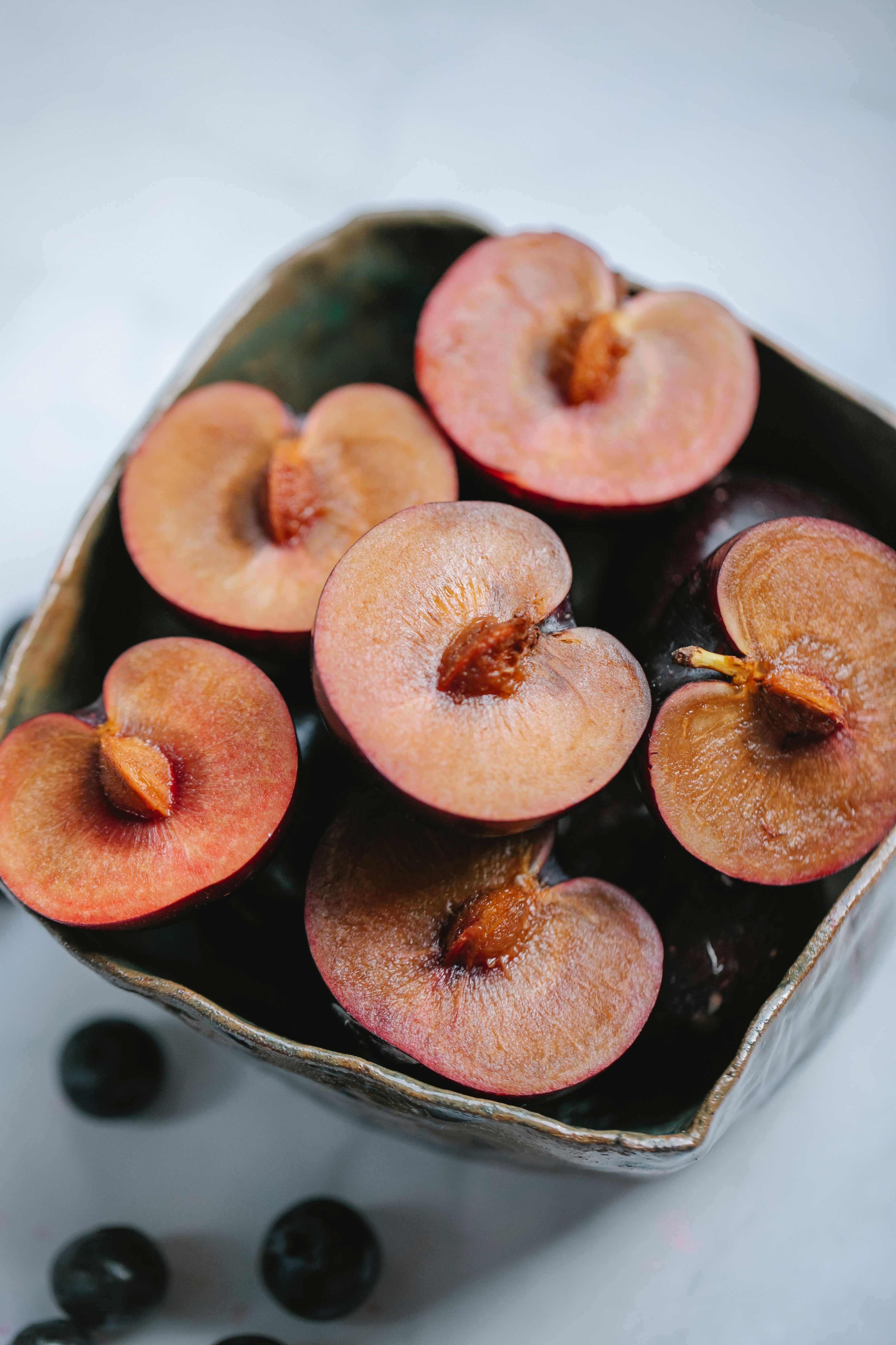 ripe appetizing halved plums in bowl served on white table