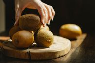 Woman taking whole unpeeled kiwi from wooden board