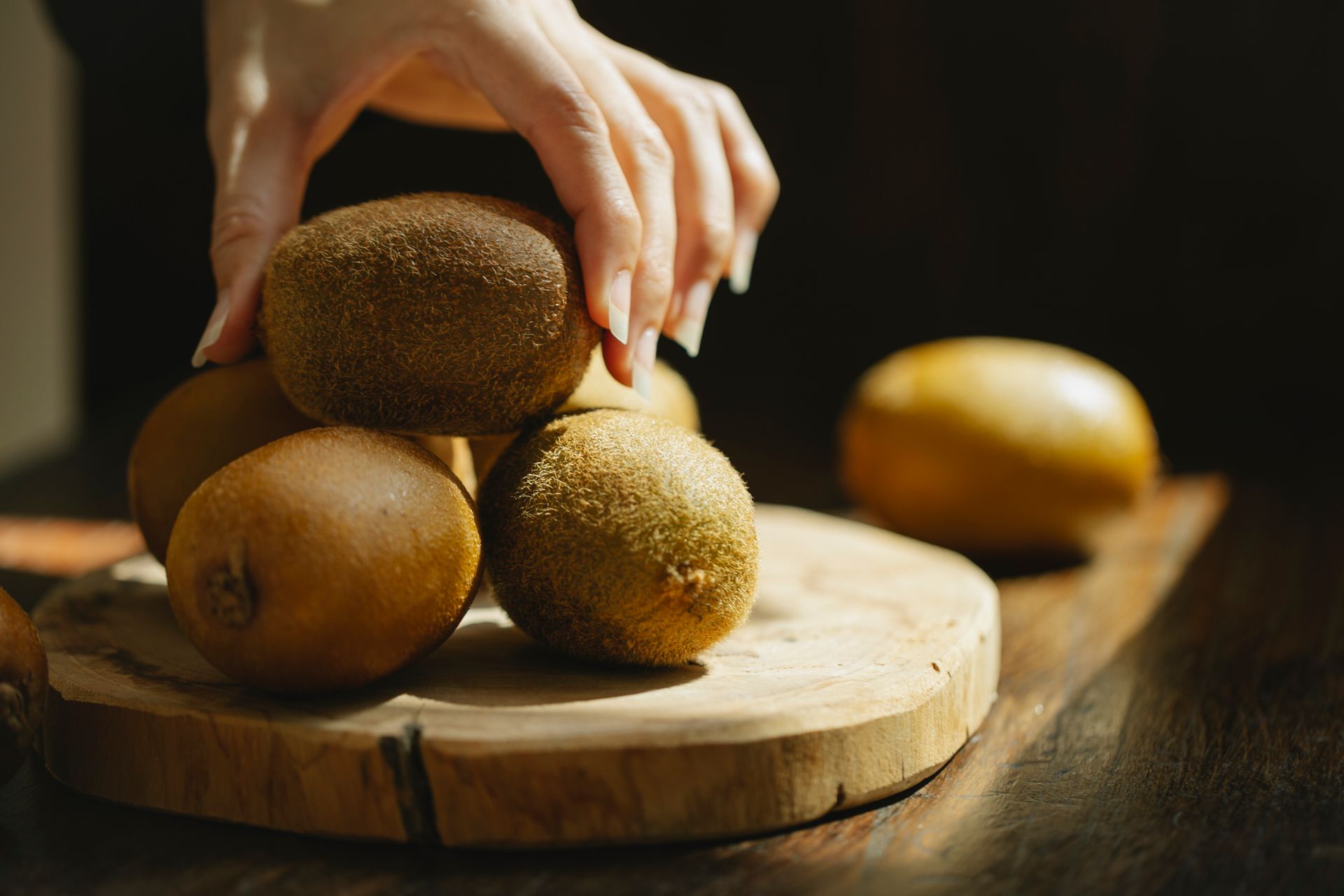 Woman taking whole unpeeled kiwi from wooden board