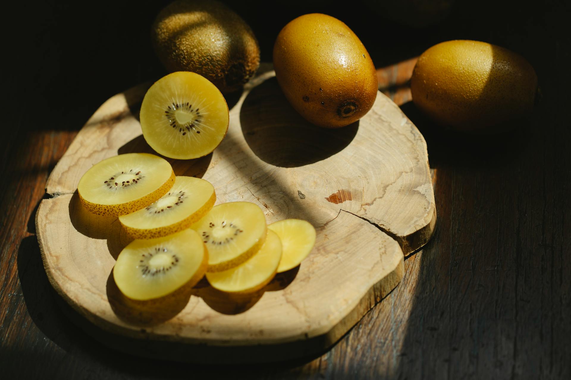 Sliced and whole kiwi on wooden cutting board