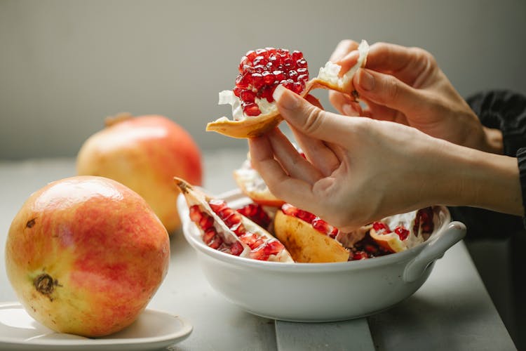 Woman Taking Off Peel From Ripe Pomegranate