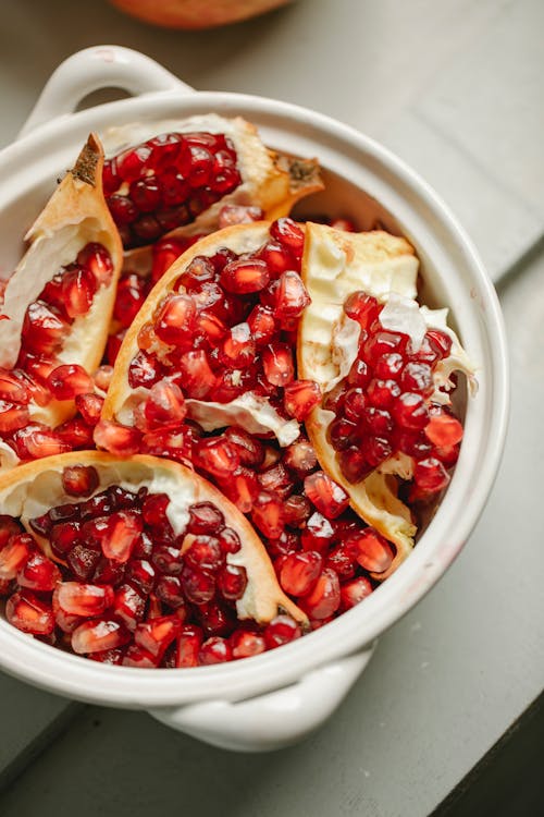 Top view of ripe pomegranate red seeds and peel placed in ceramic pot on table