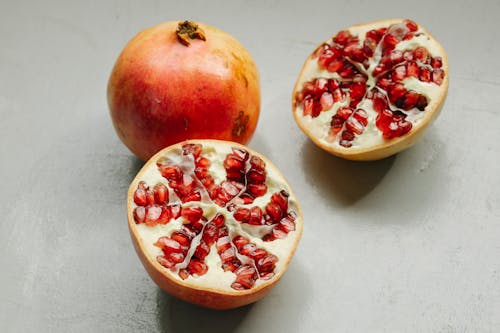 Ripe whole and halved pomegranates with red seeds placed on gray background in studio