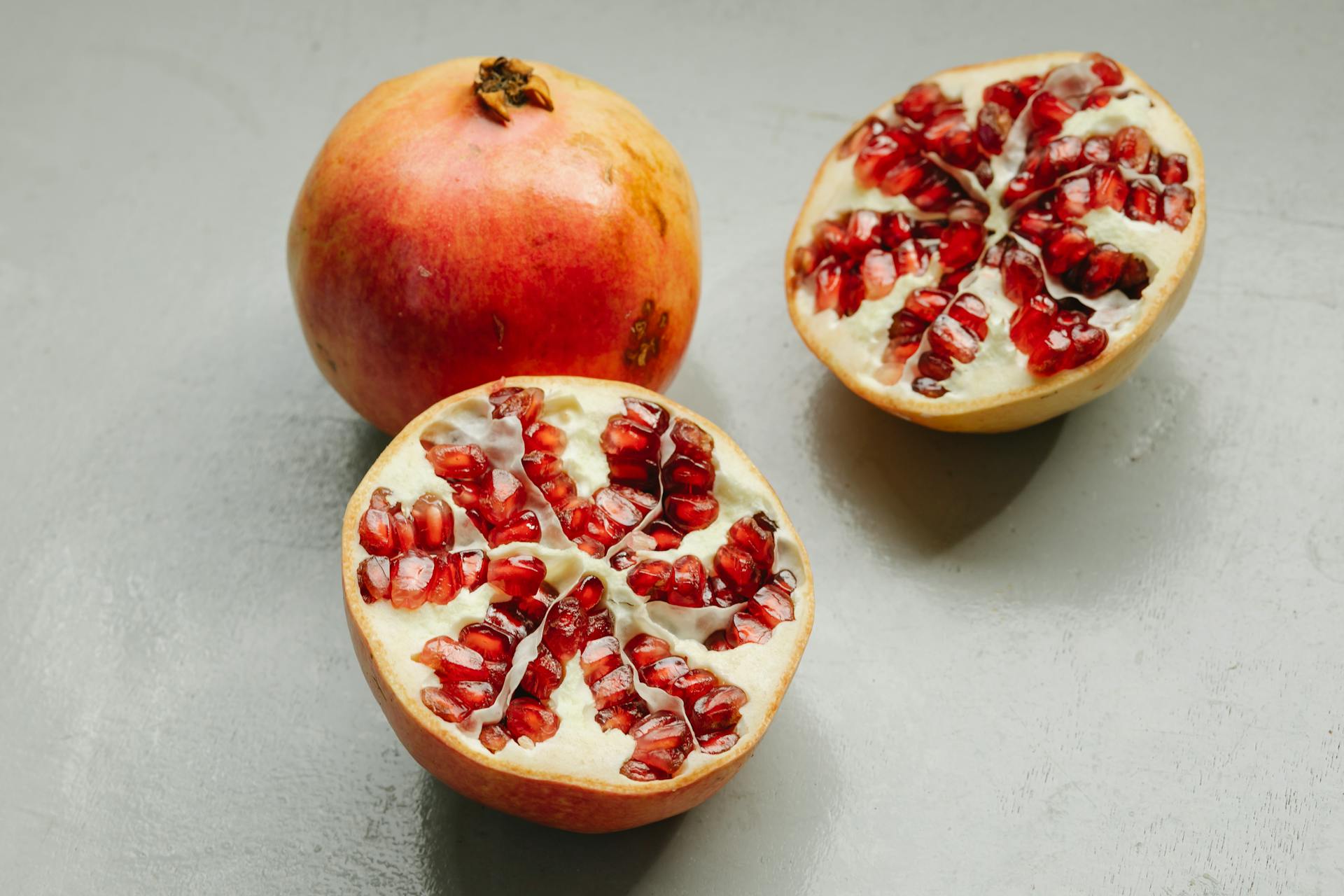 Ripe whole and halved pomegranates with red seeds placed on gray background in studio