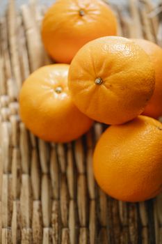 From above pile of citrus fresh orange tangerines placed on wicker surface in kitchen on blurred background