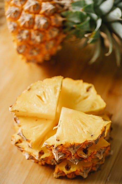 Free From above of chunks of ripe exotic pineapple placed on wooden cutting board with half of fruit on blurred background Stock Photo