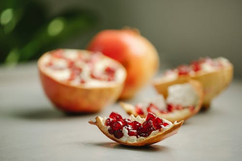 Chunk of ripe pomegranate with red seeds placed on surface near halves of tasty fruit on blurred background in kitchen